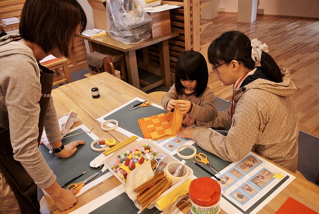 Child making a paper craft with adults at a workshop table